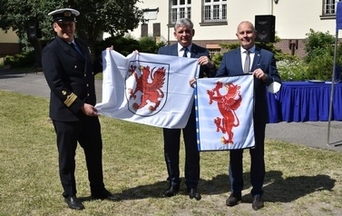 Od lewej dr hab. inż. Tomasz Neumann, profesor UMG, dziekan wydziału nawigacji, Z-ca Prezydenta Miasta Tczewa Adam Burczyk oraz Starosta Tczewski, Mirosław Augustyn pozują z flagami Miasta Tczewa oraz Powiatu Tczewskiego. 